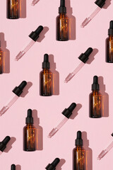 Obraz premium Simple face skincare pattern made with dark brown glass serum or essential oil bottle and dropper on pastel pink background. Minimal fresh product aesthetic.