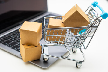 Toy shopping cart with cardboard boxes on a notebook. Consumer society trend.