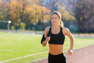 Female athlete is running in the stadium on a sunny day, woman in sportswear is active.