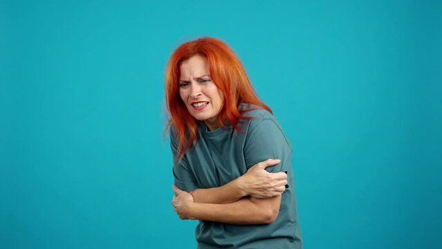 Mature redheaded woman looking at camera gesturing she is cold
