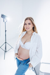 Cute pregnant woman in bra and white shirt on white background. Happy pregnant woman stroking her belly.