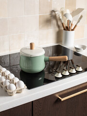Fototapeta na wymiar Saucepan on a black stove. Kitchen utensils in the background. Eggs.