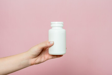 Bottle of pills or vitamins in woman's hand. White packaging for your pill or capsule and supplement