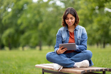 Obraz premium Smiling Young Arab Female Student Resting With Digital Tablet Outdoors