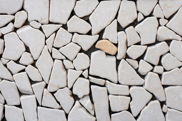Light small stones in the middle of which is a dark orange stone, one stands out among the others. The wall is laid with pebbles of various shapes, the wall is decorated with small stones