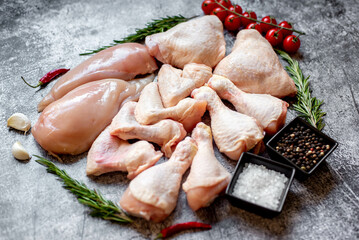 Set of raw chicken fillet, thigh, wings and legs on a stone background