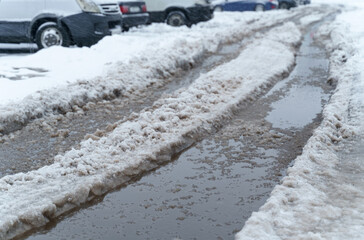 The road is covered with snow and slush, cars are parked on the side of the road.