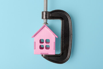 Pink house model in C-clamp on blue background