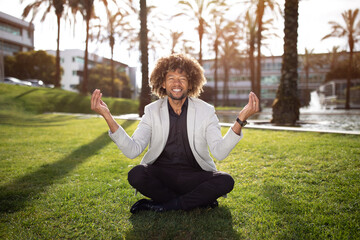 Happy black businessman meditating outdoors, sitting in park after hard working day, free space
