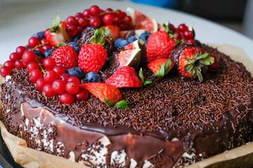 Delicious cake decorated with dark chocolate and fresh figs and blackberries, strawberries, currants. Appetizing chocolate cake with chocolate chips. Advertising for chocolate lovers. Bakery poster
