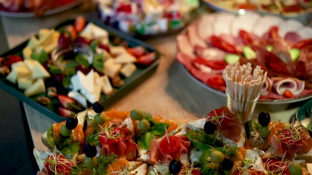fourchette table in a nightclub or restaurant with tasty delicious dishes,cheese asorti,fruits,spread with prosciutto,olive,jelly colorful cake.dark walls pour light condition 4k rotating spinning