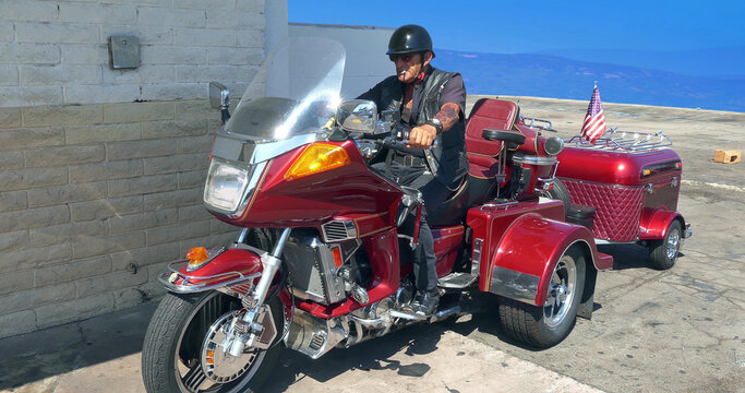 Veteran biker with cigarette on the Three-Wheeled motorcycle departs from parking lot in Los Angeles, California