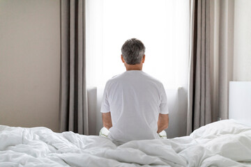 Back view of man sitting on bed, looking through window
