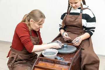 Woman and little girl working with clay in a pottery workshop. Craft, art and hobbies concept. Teacher of handcraft showing a pupil how to make clay mug during lesson in workshop
