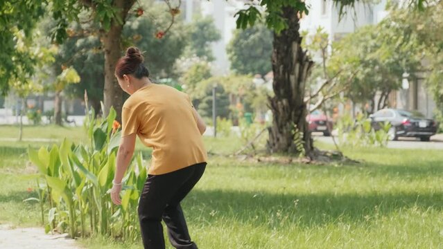 Mature Asian woman playing badminton with husband while spending summer day in park