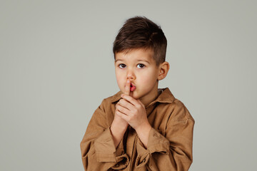 Mystery serious funny caucasian 6 years old little boy show with finger shhh sign isolated on gray...