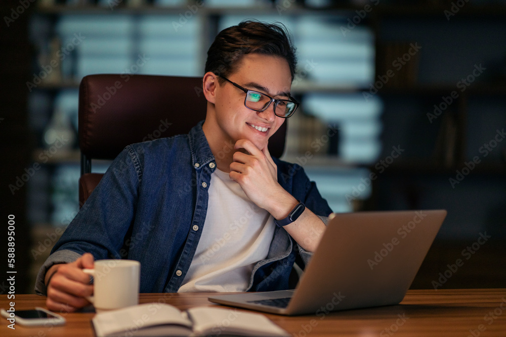 Poster employee looking at computer screen and smiling, drinking coffee