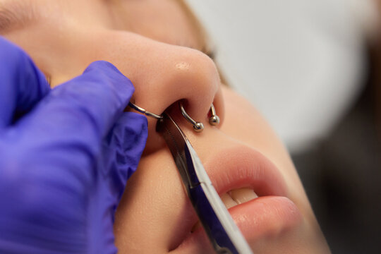 Young woman doing piercing nose ring at beauty studio salon.