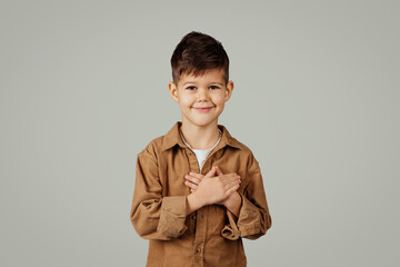 Cheerful caucasian 6 years old little boy in casual presses hands to heart, say thanks