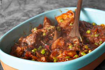 Beef casserole, with potato, broccoli, peas and onion, in a tomato and red wine sauce, Served in a casserole dish on a dark stone background