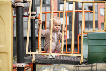 A small Child Alone plays on the children's playground in the yard.