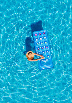 Top view of a young female in a straw hat on blue swimming pool waves background with blue inflatable mattress. Chill out a summer vacation in luxury resorts concept.