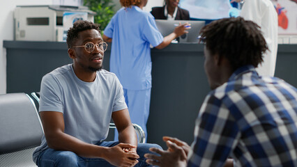 Group of people sitting in waiting room at hospital and talking about medical insurance support. Male patients waiting to attend examination, discussing about treatment or medicine.