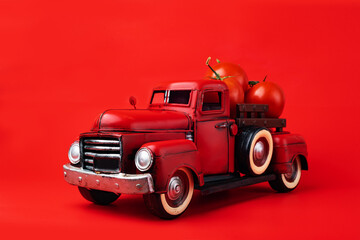 Red retro pickup truck carries fresh tomatoes on a red background, harvesting, and creative presentation of the product.