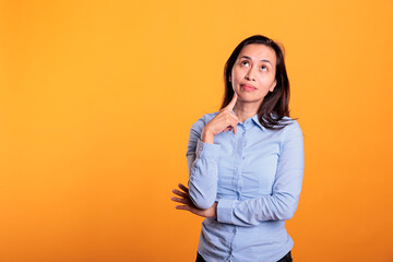 Filipino woman thinking with finger on chin in front of camera in studio. Thoughtful model feeling...
