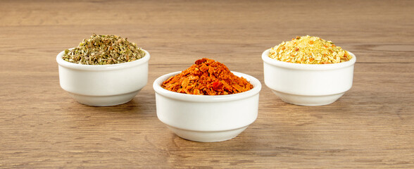 Three white saucers with various seasonings of a bright color are arranged in a triangle on a wooden table.