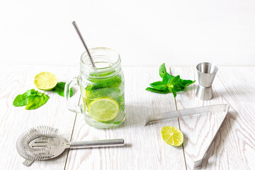 Fresh iced cold mojito lemonade summer drink, cocktail with sliced lime, bright green mint leaves and frozen ice cubes in a transparent cup, mason jar on wooden table