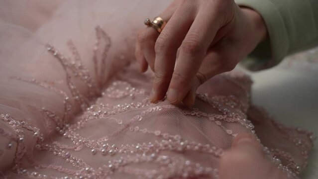 A seamstress decorates a dress with beads and sequins