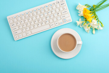 Computer keyboard and coffee cup on turquoise table with freesia flowers. Top view, flat lay, copy space