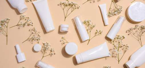 White plastic tubes, jars, and gypsophila branches on a beige background, containers for cosmetic creams and gels, advertising and brand promotion, top view