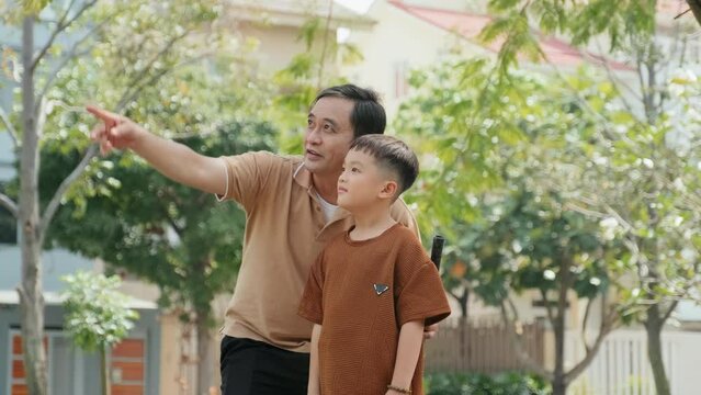 Tilt up shot of Asian father teaching son how to hold badminton racket and explaining rules of game in park on summer day
