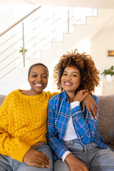 Happy diverse female lesbian couple embracing sitting on sofa
