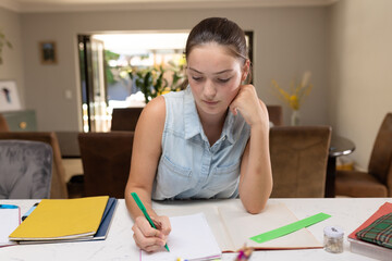 Obraz na płótnie Canvas Caucasian teenager girl sitting at table and doing homework