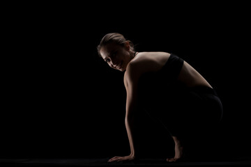 cute caucasian girl exercising yoga poses against dark backgroung. side lit silhouette...