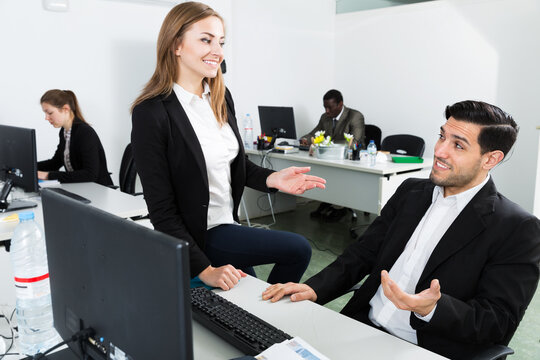 Positive young business woman flirting with man working at laptop in office