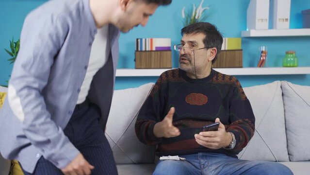 Son helping father who can't pay the bill on the phone.
The son shows his father how to pay bills on the phone. The failing father is pleased and thanks.
