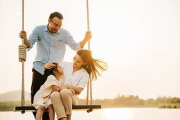 A happy family playing together on a swing set in a beautiful park, with the parents and children...