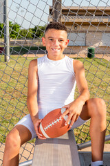 Male youth 7 on 7 football player smiling and sitting while holding his football