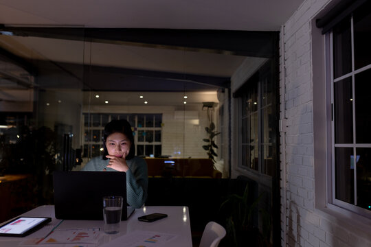 Asian businesswoman sitting at desk and using laptop, working late at office