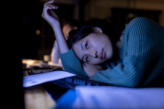 Tired asian businesswoman sitting at desk and using computer, working late at office