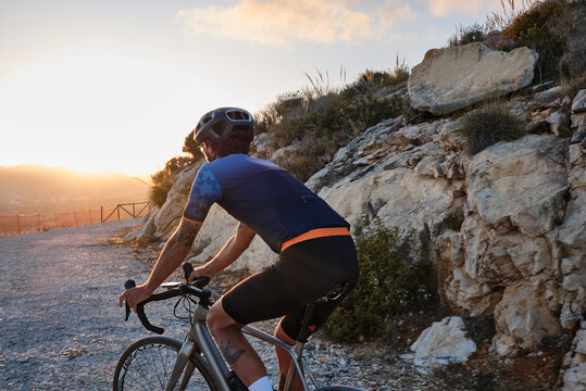 Fit male cyclist in cycling kit and helmet riding gravel bike on scenic gravel road during sunset in Spain.Gravel road in mountains.Sport motivation.Calp, Alicante, Spain