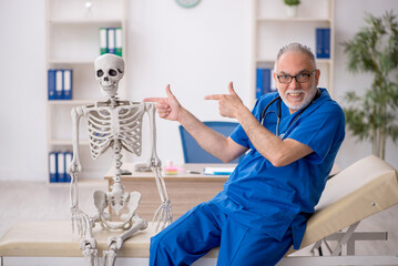 Old male doctor examining skeleton in the clinic