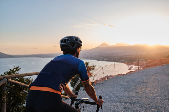 Fit male cyclist in cycling kit and helmet riding gravel bike on scenic gravel road during sunset in Spain.Gravel road in mountains.Sport motivation.Calp, Alicante, Spain