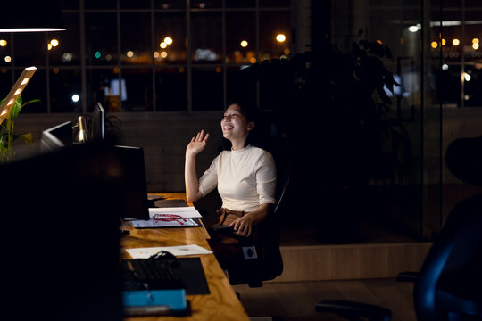 Happy asian businesswoman sitting at desk, using computer for video call, working late at office