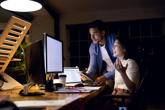 Diverse happy business people using computer with copy space on screen, working late at office