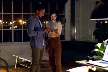 Diverse business people using tablet together and discussing, working late at office